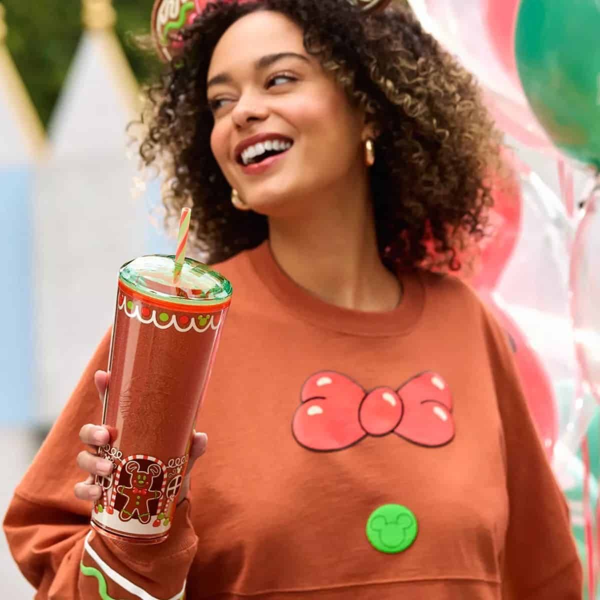 Someone in a gingerbread sweatshirt holding a gingerbread Mickey tumbler with a candy-cane straw