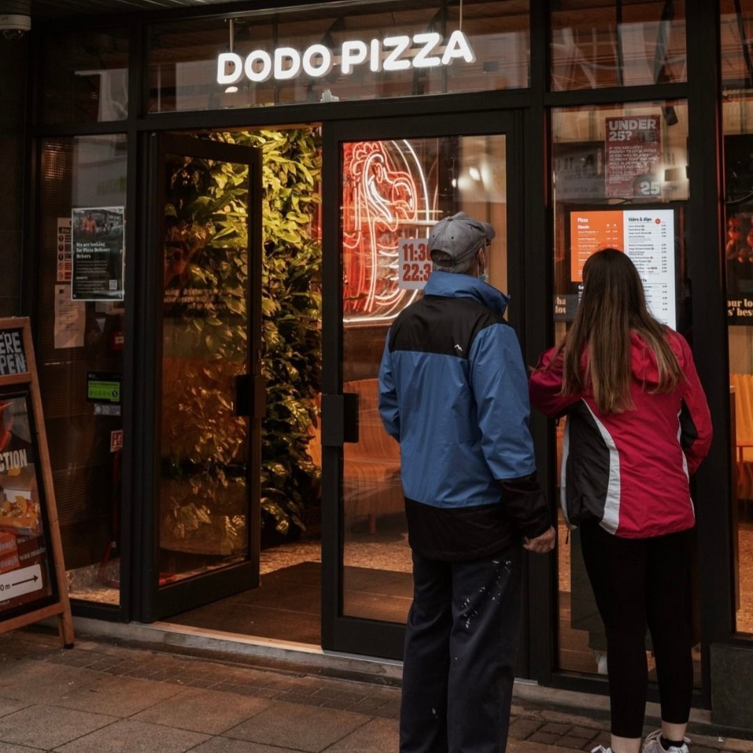 Two people reading the menu in the window of a Dodo Pizza UK restaurant