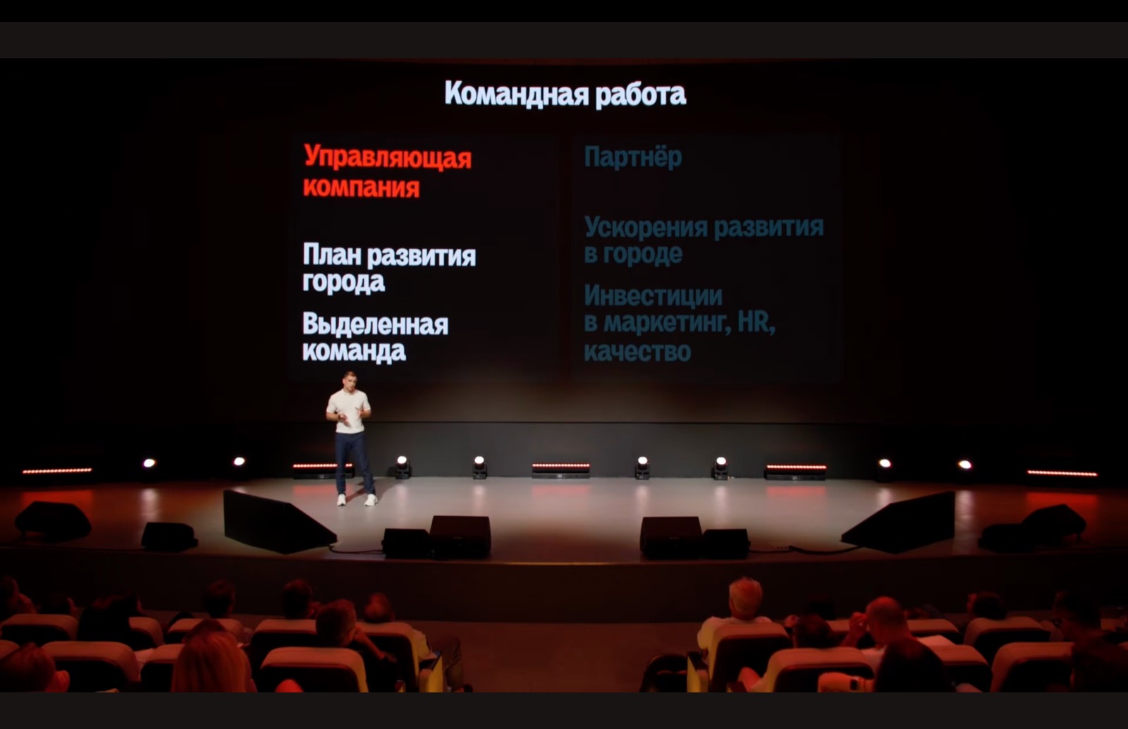 Speaker on stage in front of a Teamwork slide comparing the roles of the management company and the partner