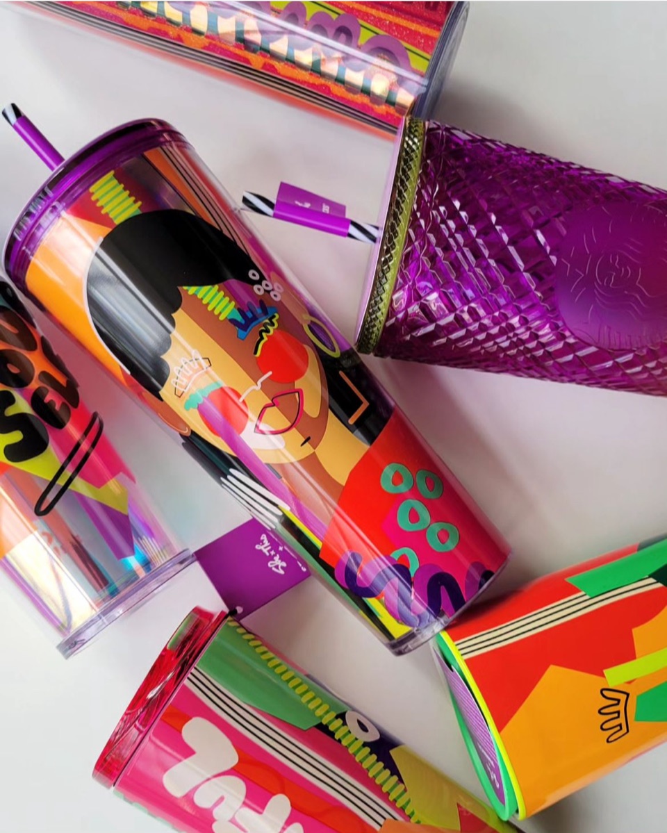 “She Is This” cold cups and a purple studded tumbler laid out together